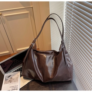 Detailed view of the dark brown pleated tote bag on a desk with warm natural lighting