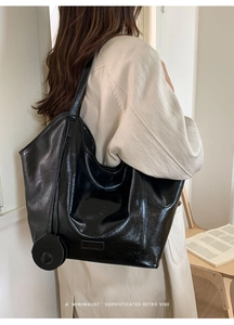 Detail showing high-gloss black leather tote bag with a minimalist retro pendant charm