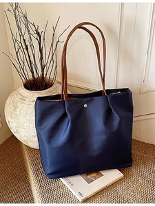 Large dark blue tote bag with brown leather straps displayed on a rustic staircase