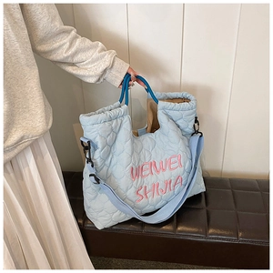 Close-up of light blue quilted tote bag with pink embroidery and navy handles