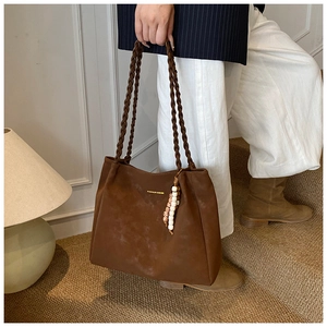 Detail of a large brown tote bag with woven handles and a decorative wooden bead charm