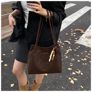Close-up of deep brown suede tote bag with woven handles and colorful bead charm decoration