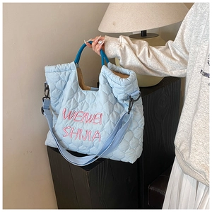 Detail of light blue quilted tote bag featuring pink letter embroidery and nylon texture