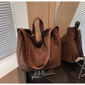 Detailed view of brown checkered canvas tote bag with shoulder straps on a wooden table