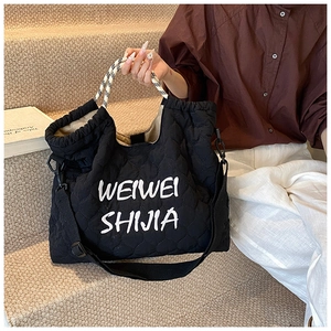 Detail of black quilted tote bag with white logo and adjustable woven shoulder strap