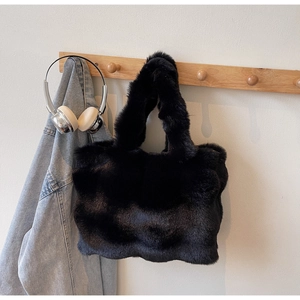 Gros plan du sac cabas en peluche noire suspendu à des crochets en bois avec un jean