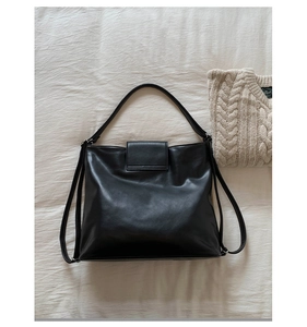 Detail of minimalist black leather tote bag on beige fabric with cozy autumn knitwear
