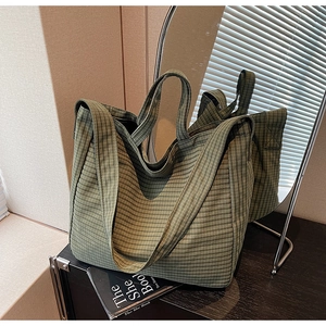 Detail of dark green plaid canvas tote bag with top handles on dark wooden cabinet