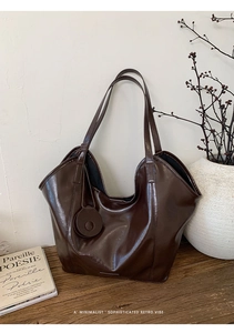 Detail of a dark brown glossy tote bag with dual straps and a decorative round charm