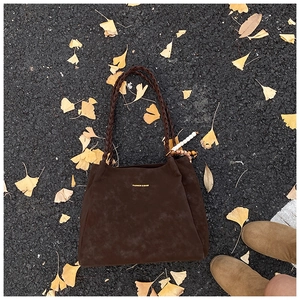 Close-up of brown suede tote bag with woven straps and bead detail on autumn leaves