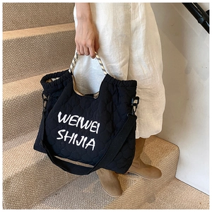 Detail of black quilted nylon tote bag featuring woven handles and printed logo lettering