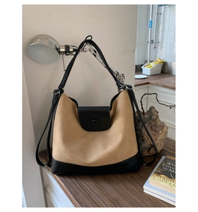 Detail of the high-capacity tote bag showing beige suede texture and black leather straps