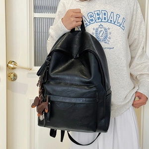 Detail of black faux leather backpack featuring textured finish and cute dog charm
