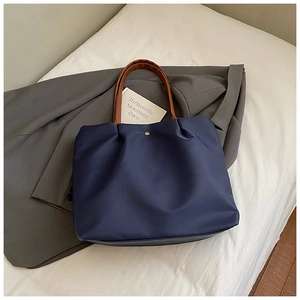 Detail of dark blue tote bag featuring brown handles and golden metal buckle closure