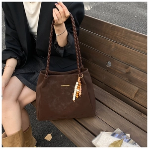 Detailed close-up of dark brown suede tote bag with woven handles and beaded charm decor