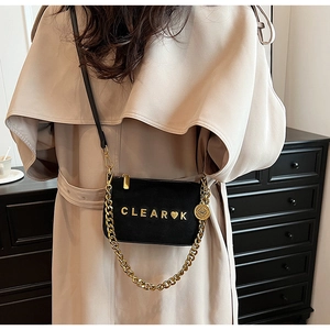 Detail of black matte crossbody bag with gold chain strap and heart logo on shoulder