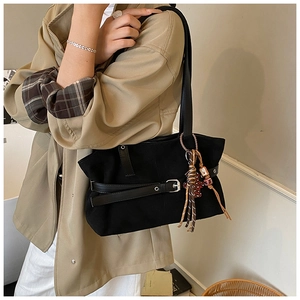 Detail of black canvas tote bag featuring leather straps and leopard print charm