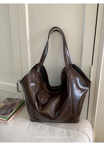 Macro detail of dark brown polished leather tote bag with subtle logo and round charm