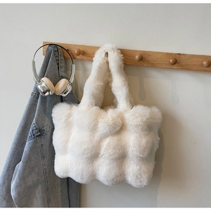 Gros plan d'un sac cabas en fausse fourrure blanche matelassé suspendu à un crochet en bois