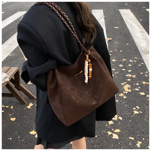Detail of dark brown suede tote bag with woven strap and beaded tassel in autumn setting