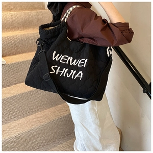 Detail of black quilted tote bag featuring white cursive embroidery and broad shoulder strap
