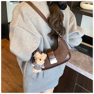 Detailed back view of a brown crescent shoulder bag featuring a cute plush dog pendant