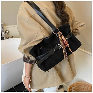 Close-up of black suede tote bag featuring silver buckle and colorful tassel charm
