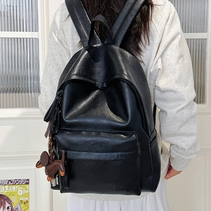 Detail of black faux leather backpack featuring Hoog embossed logo and dog charm detail
