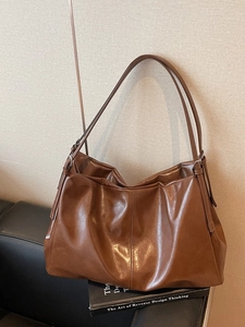Brown faux leather oversized tote bag with dual shoulder straps on a black leather sofa