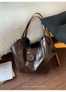 Detail of dark brown glossy leather tote bag with round charm in a cozy home setting