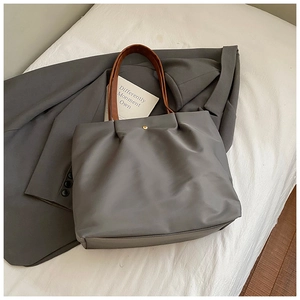 Detail of grey minimalist tote bag featuring brown straps and a golden snap closure