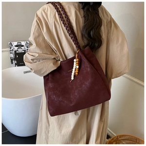 Detail of burgundy tote bag with braided handles and decorative bead tassel charm