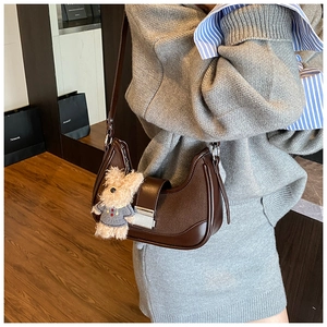 Detail of dark brown crescent bag with silver buckle and plush bear charm on a model