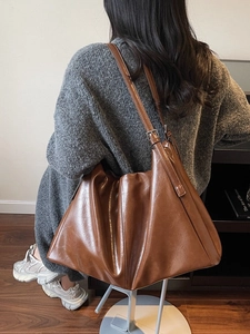 Brown leather hobo tote bag with adjustable strap worn by model in casual style