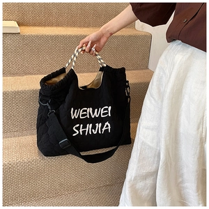 Detailed close-up of a black quilted tote bag with woven handles and brand lettering