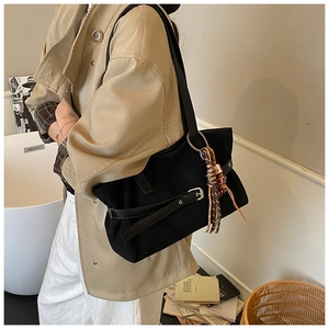 Detail of black canvas tote bag with leather strap, silver buckle and tassel charm