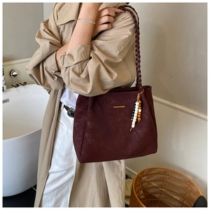 Detail of burgundy tote bag with woven strap and beaded charm on autumn trench coat