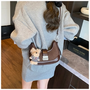 Detail of dark brown crescent bag with plush bear charm and silver buckle strap