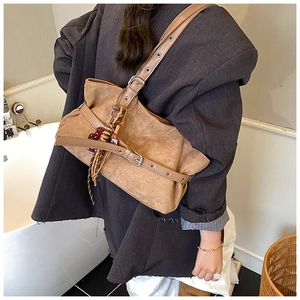 Detail of dark brown suede tote bag featuring metallic buckle straps and tassel accents