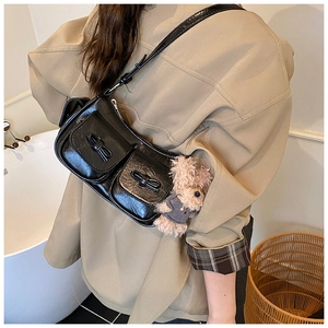 Detail of black glossy shoulder bag featuring dual pockets with bows and a bear charm