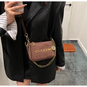 Detail of a brown matte suede crossbody bag with gold chain and heart logo lettering