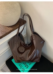 Detail of dark brown glossy tote bag with round charm and branding on interior bottom