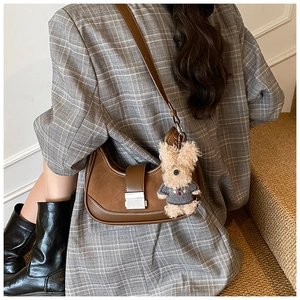 Close-up of brown leather and suede saddle bag featuring a silver lock and plush dog charm