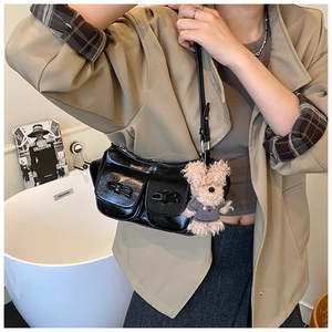 Detail der schwarzen glänzenden Schultertasche mit Doppeltaschen und süßem Bärenanhänger