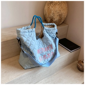 Detailed view of light blue quilted nylon tote bag with pink embroidery on stone steps