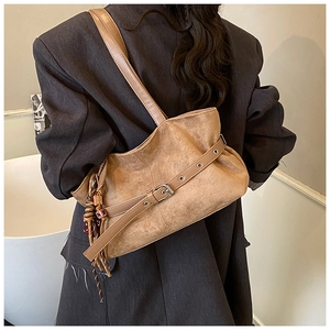 Close-up of caramel suede shoulder bag with decorative buckle and bohemian tassel charm