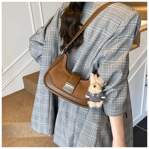 Detail of a brown crescent shoulder bag with a matte finish and a cute plush puppy pendant