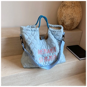 Detail of light blue quilted tote bag with pink embroidery on stone steps