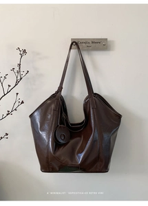 Polished dark brown hobo bag with oily leather texture hanging on a minimalist wall
