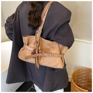 Detailed close-up of brown suede shoulder bag with heart charm on female model